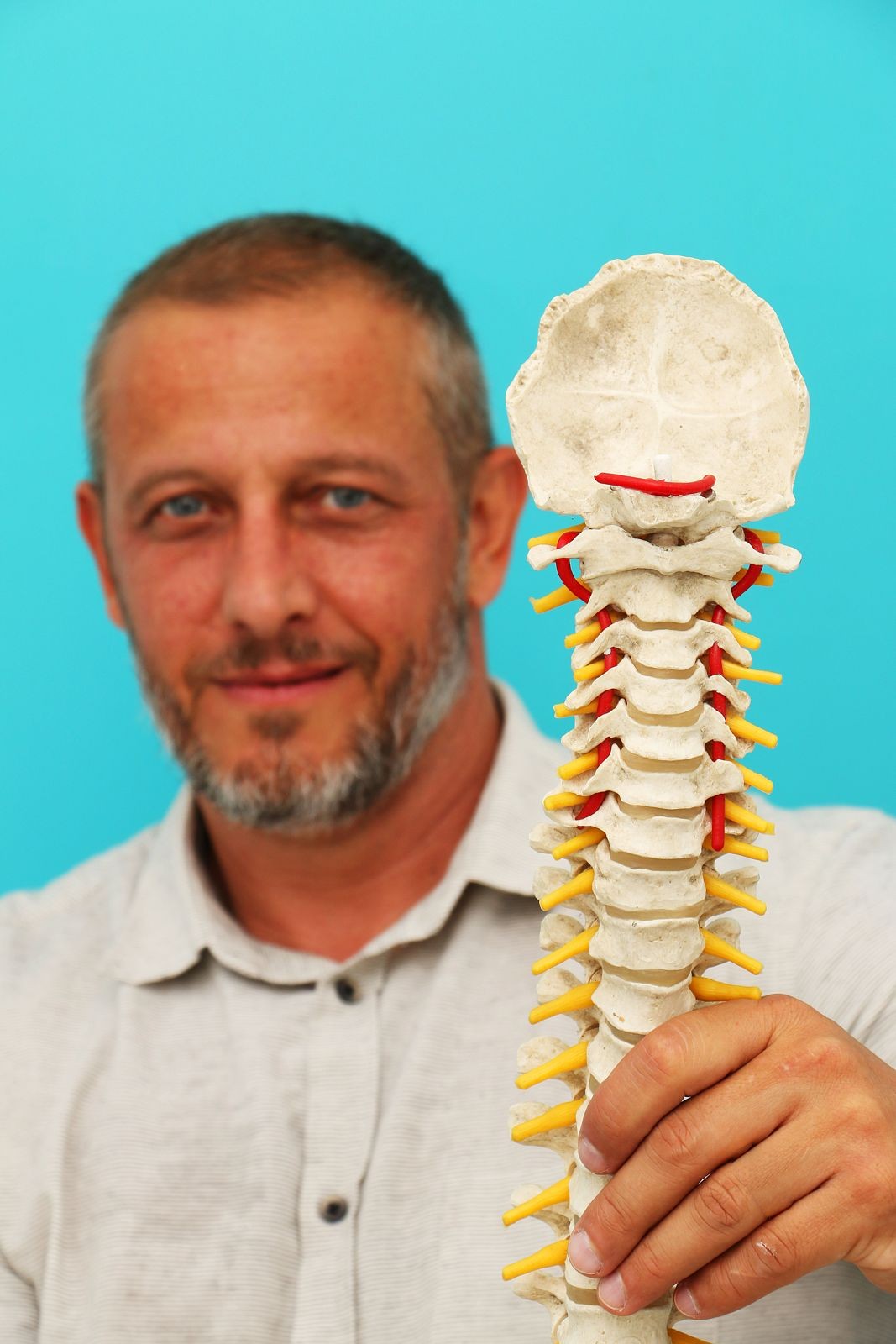 Alexandre Zuppo, quiropraxista, segurando um modelo de coluna vertebral diante da parede turquesa do consultório